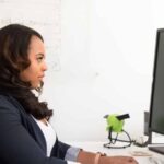 This photo shows a lady working in from on 2 screens to depict someone working with computers and who is likely to have several passwords they use every day. thumbnail
