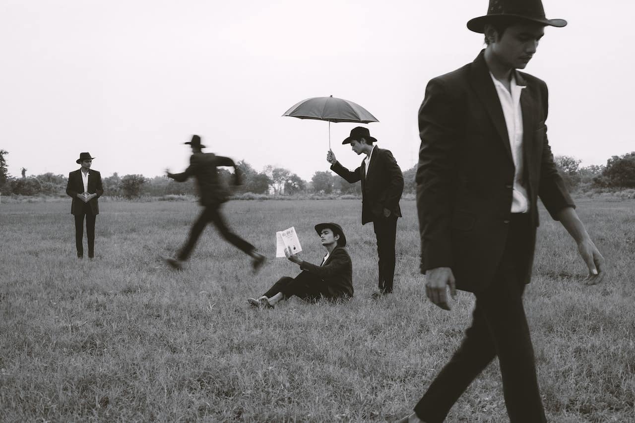 This photo shows a business person appearing several times on a grass landscape. He is wearing a suit and a hat, sometimes appearing with an umbrella, paper or running. This photo depicts the typical mortgage broker chasing after clients to get the information needed to work out the best finance options for the client.