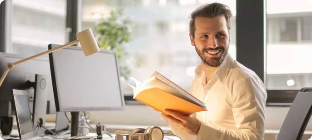 This image shows a man sitting at a desk. He is turning around with a book in his hands, smiling at us, presumably showing that Gatheroo is making his mortgage broker business more efficient and making him happy happy.
