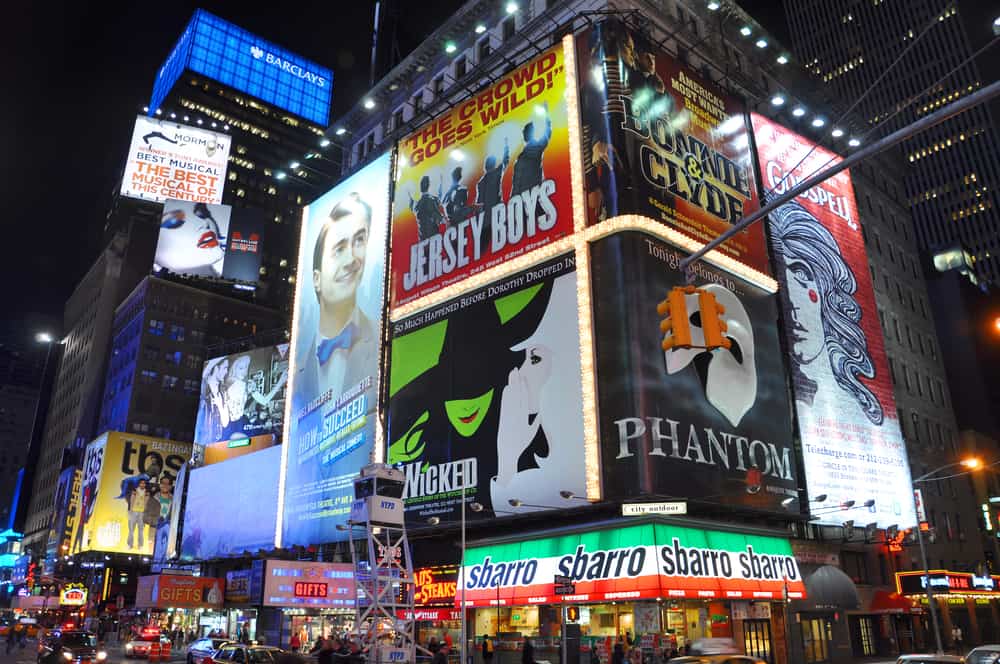 This photo shows several musical advertising posted on Broadway in New York, at night.