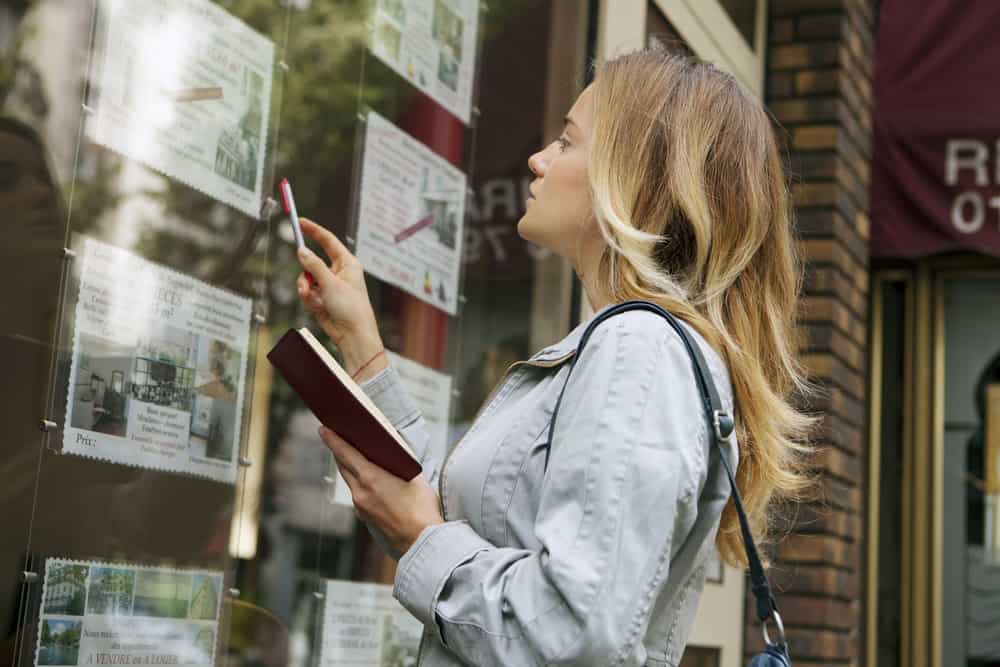 This photo shows a lady looking at real estate photos in a window with a clipboard in her hands. This compliments the theme of this article which is about how Gatheroo helps Mortgage Brokers to collect information and documents from their clients.