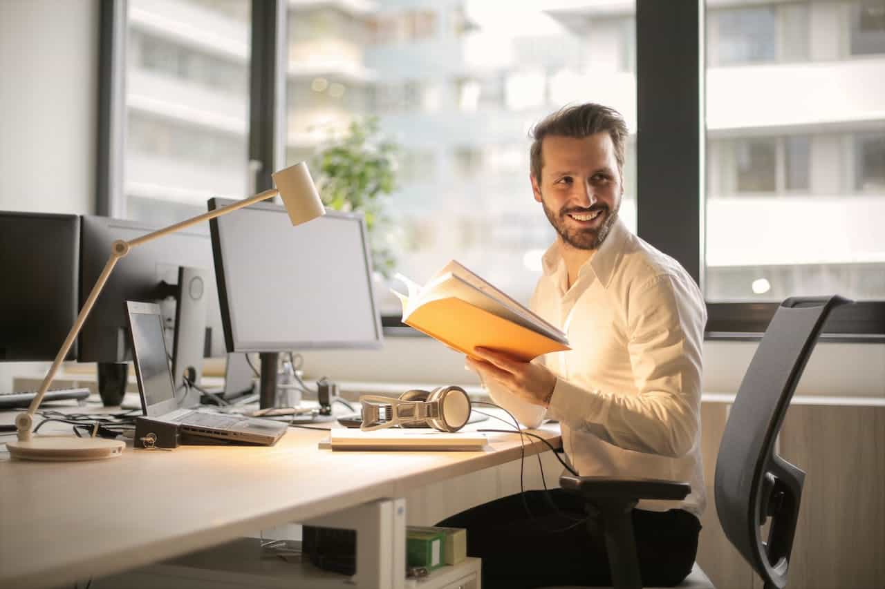 This image shows a man sitting at a desk. He is turning around with a book in his hands, smiling at us, presumably showing that Gatheroo is making his mortgage broker business more efficient and making him happy happy.