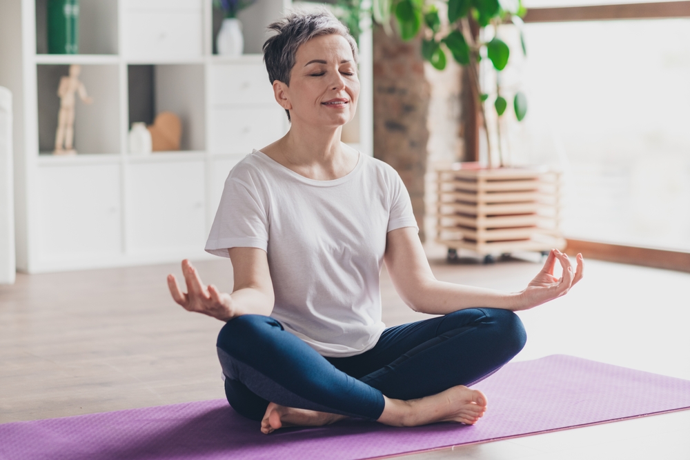 Jane, a bookkeeper, is using Gatheroo and has now found time for self-care, she is shown here in a meditating pose on a dark purple yoga mat