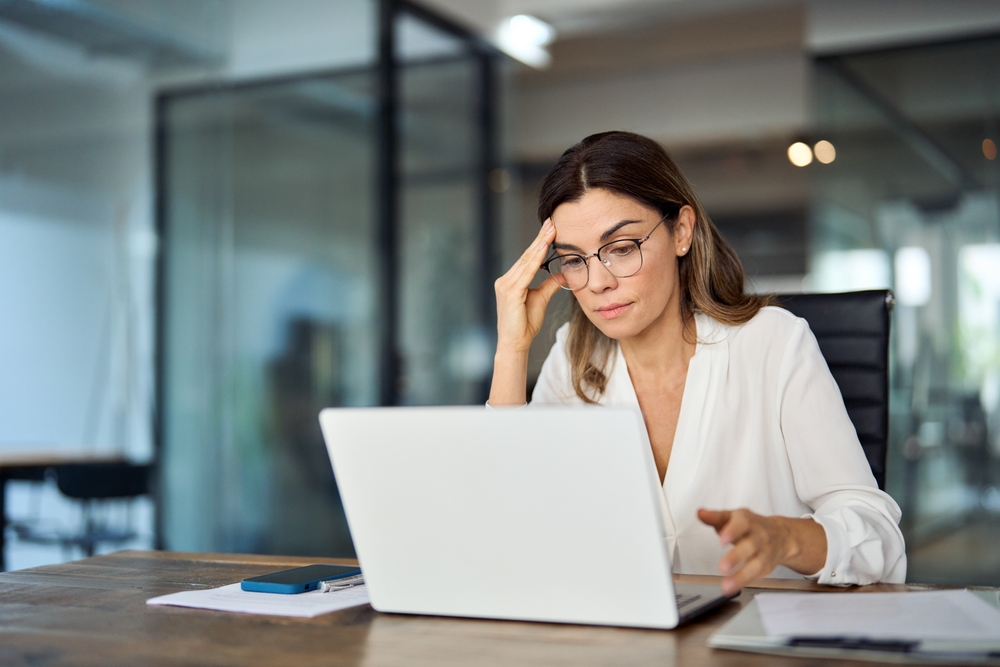 Bookkeeper Kylie is sitting in front of her laptop with her head resting on the fingertips of her right hand, as she looks annoyed with what she sees